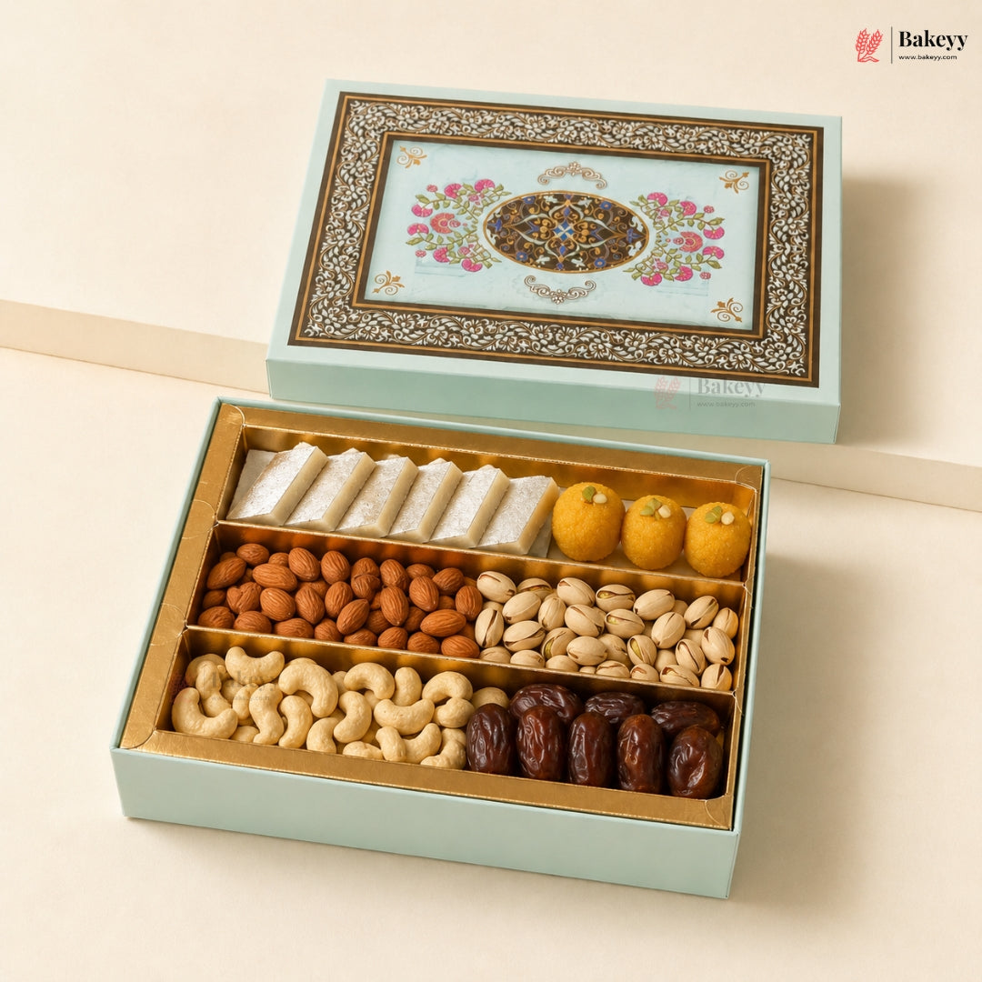 An open light blue gift box filled with assorted dried fruits and nuts, including white sweets, almonds, pistachios, cashews, and dates, with a decorative illustrated lid shown above on a beige background. Bakeyy branding is visible.