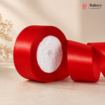 Red satin ribbon roll on a light wooden surface with 'Bakeyy' branding.