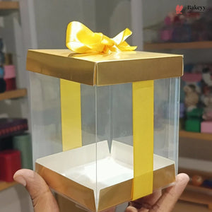 Clear gift box with gold accents and a yellow bow held by a person.