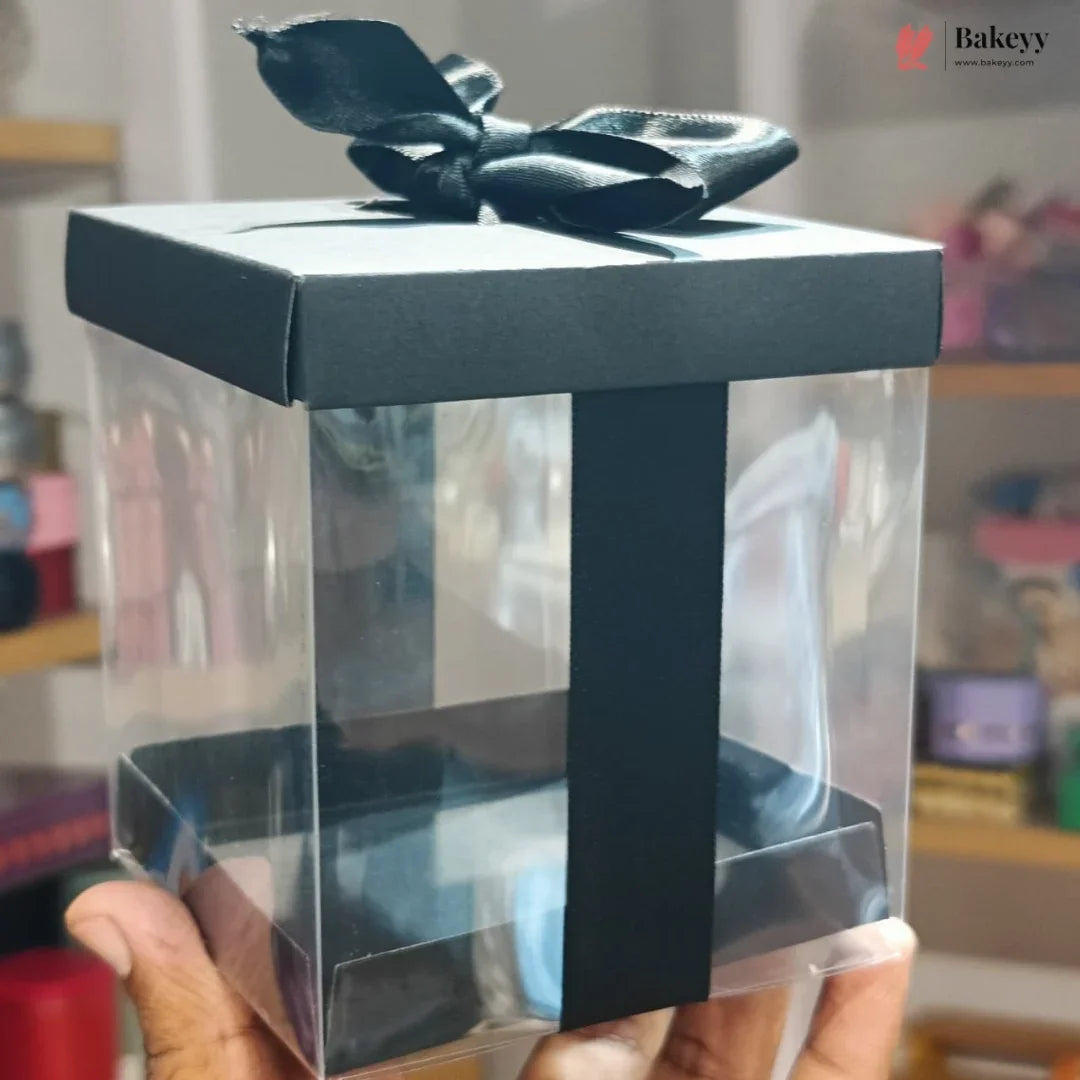Clear gift box with black ribbon held by a hand, blurred background
