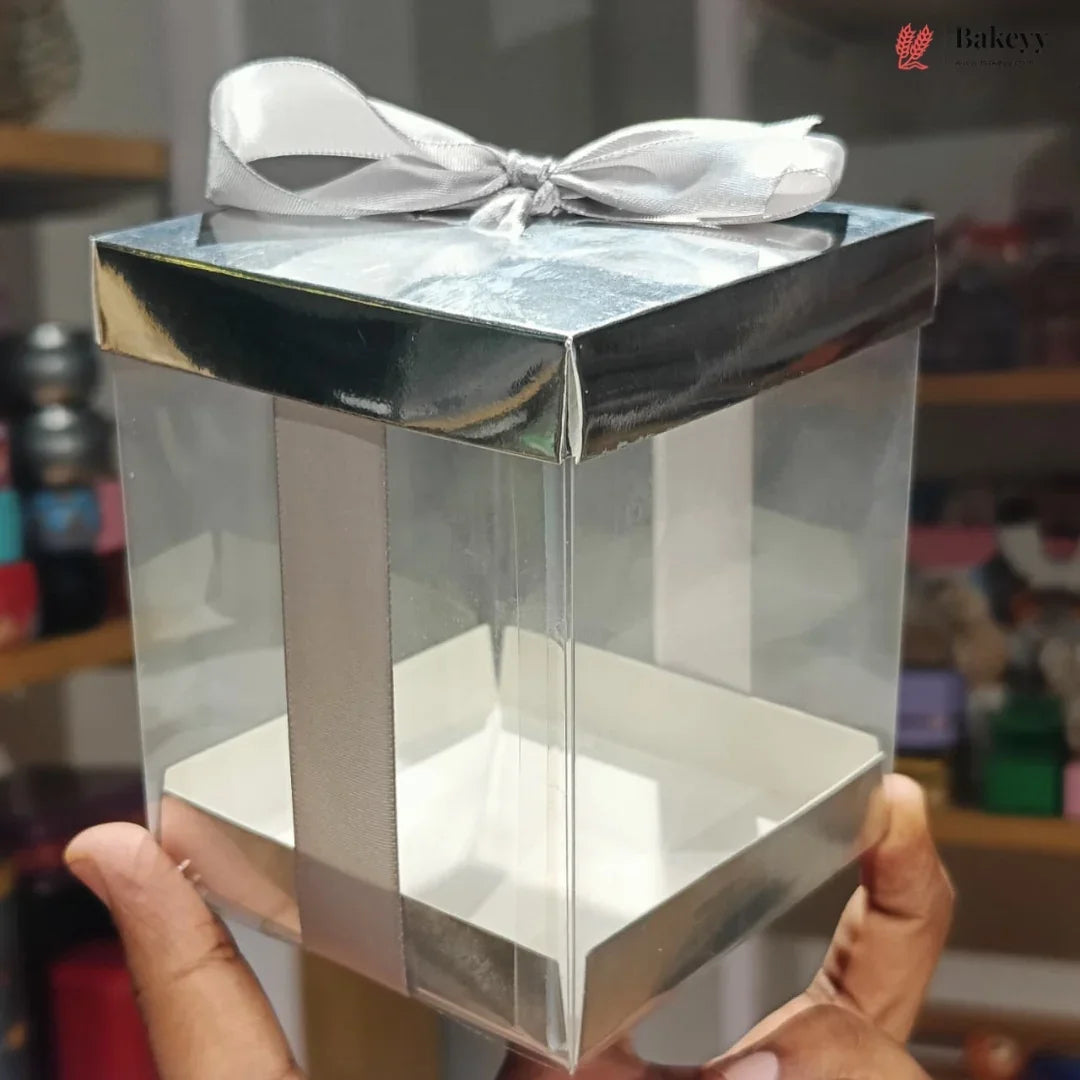 Clear gift box with a silver bow held by a hand against a blurred background