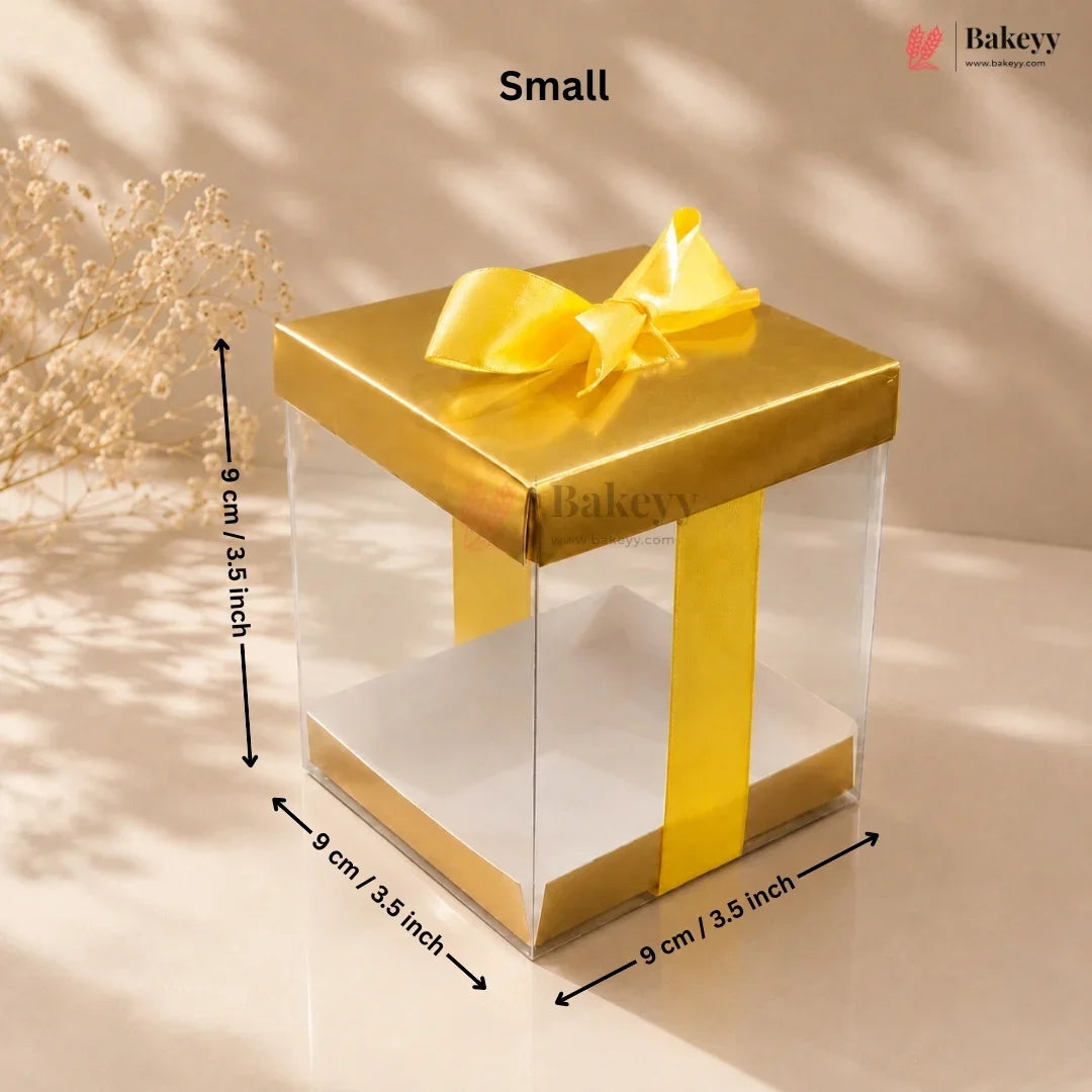 Gold gift box with a clear side panel and dimensions on a beige background