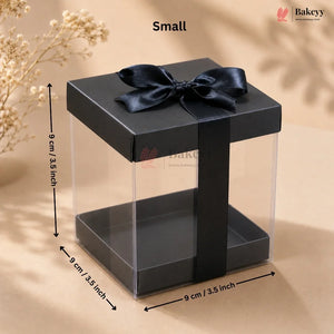 Black gift box with clear window and black ribbon, dimensions indicated, on a beige background.