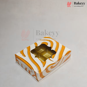 A square bakery box with a white and orange wavy pattern, featuring a clear window showing gold foil cupcake liners inside, set against a light gray background with a Bakeyy watermark.