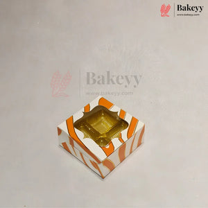 A square bakery box with a clear plastic window on top, decorated with orange and white diagonal stripes, shown on a light gray background with Bakeyy branding.