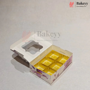 A bakery box with a hinged lid, featuring a floral pattern in purple and pink on a white base, with six gold foil compartments inside. The box is shown open on a light gray background with Bakeyy branding.