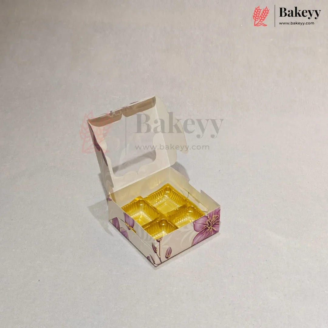 A small open bakery box with a clear window and a yellow tray inside, decorated with a purple floral pattern on a light beige background. The Bakeyy logo is visible in the top right corner.