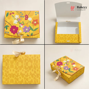 A four-panel product presentation of a yellow bakery gift box set by Bakeyy. The set includes a closed box with a colorful floral print and ribbon bow, an open box with a clear window, a flat patterned lid, and a third closed view showing the floral print on top.