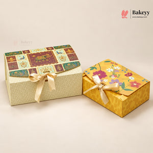 Two decorative gift boxes from Bakeey on a warm off-white background. The larger box on the left has a patchwork floral lid with a cream patterned base and a cream ribbon bow.