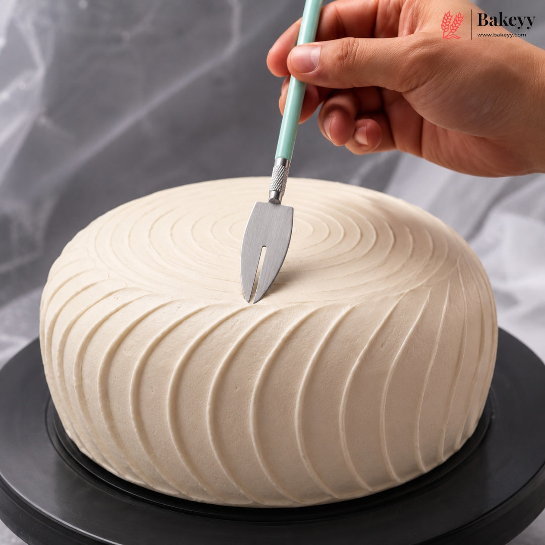 A hand holds a cake server above a round, cream-colored frosted cake on a black rotating stand, with a gray draped fabric background. A 'Bakeyy' watermark is visible in the top right corner.