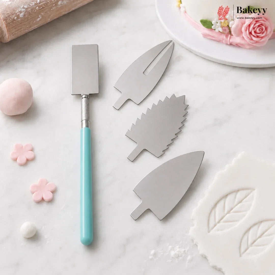 Three stainless steel cake decorating molds with leaf and flower shapes, shown alongside a turquoise-handled spatula on a white marble surface with baking props.