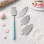 Three stainless steel cake decorating molds with leaf and flower shapes, shown alongside a turquoise-handled spatula on a white marble surface with baking props.