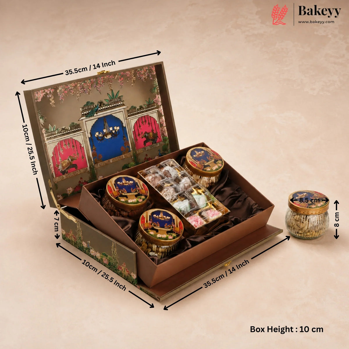 An open decorative gift box filled with assorted packaged sweets and jars, shown with dimension arrows and text indicating measurements. A small matching jar sits to the right on a warm beige textured background.
