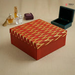 Red and gold patterned box on a beige surface with perfume bottles in the background