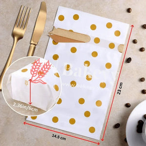 White paper napkin with gold polka dots, cut into a leaf shape, on a beige surface with coffee beans and cutlery.