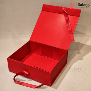 An open red gift box with a matching red ribbon handle, photographed on a neutral light gray background. The brand name Bakeyy is visible as a watermark in the top right and on the bottom right.