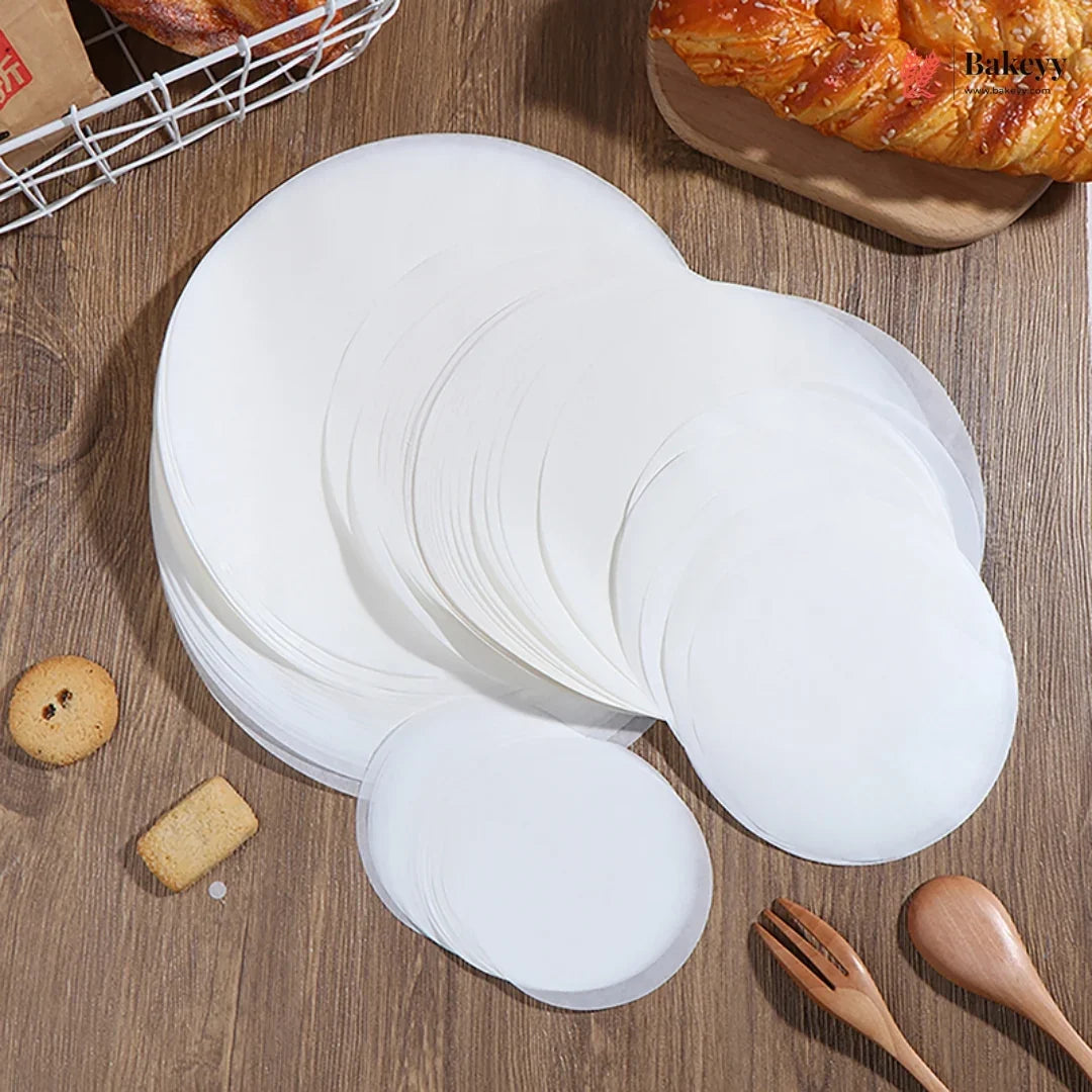 Stack of white paper plates on a wooden surface with pastries and utensils.