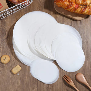 Stack of white paper plates on a wooden surface with pastries and utensils.