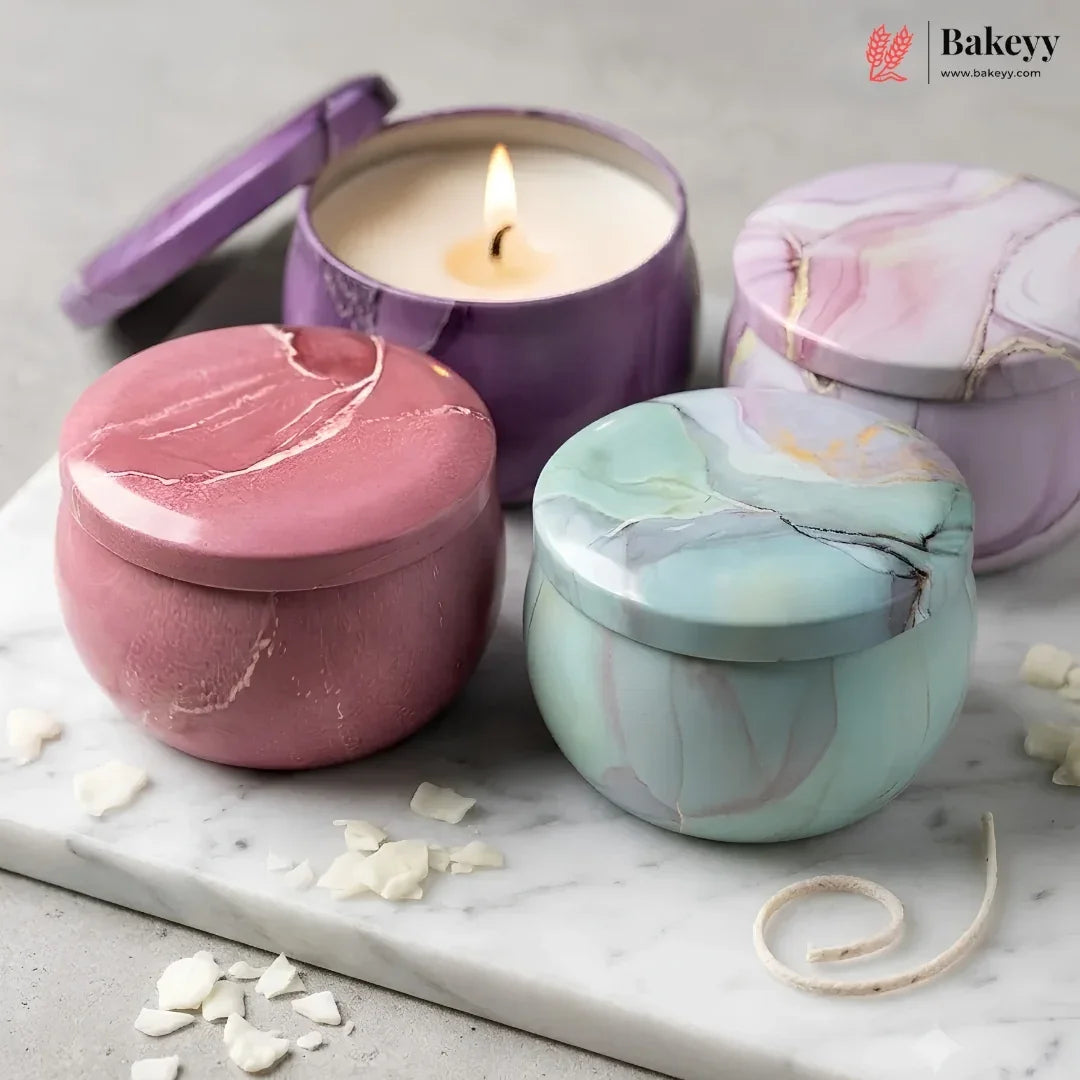 Three marbled metal candle tins with matching lids arranged on a white marble board. One tin is open and lit, showing cream wax and a small flame.