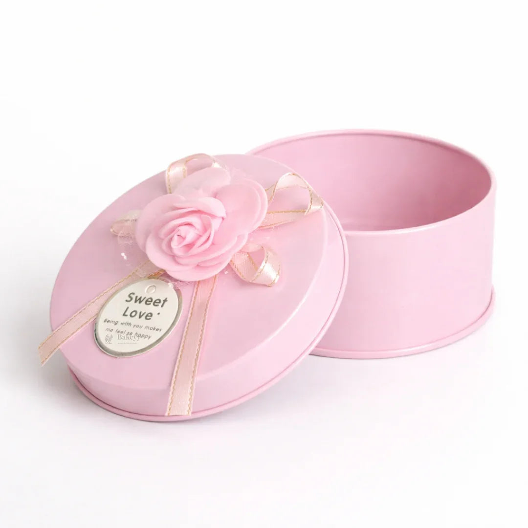 Pink round metal tin box with ribbon and flower, perfect for gift packaging from Bakeyy.com