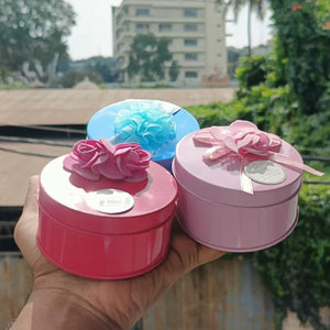 Hand holding three round decorative metal tin gift boxes with ribbon flowers from Bakeyy