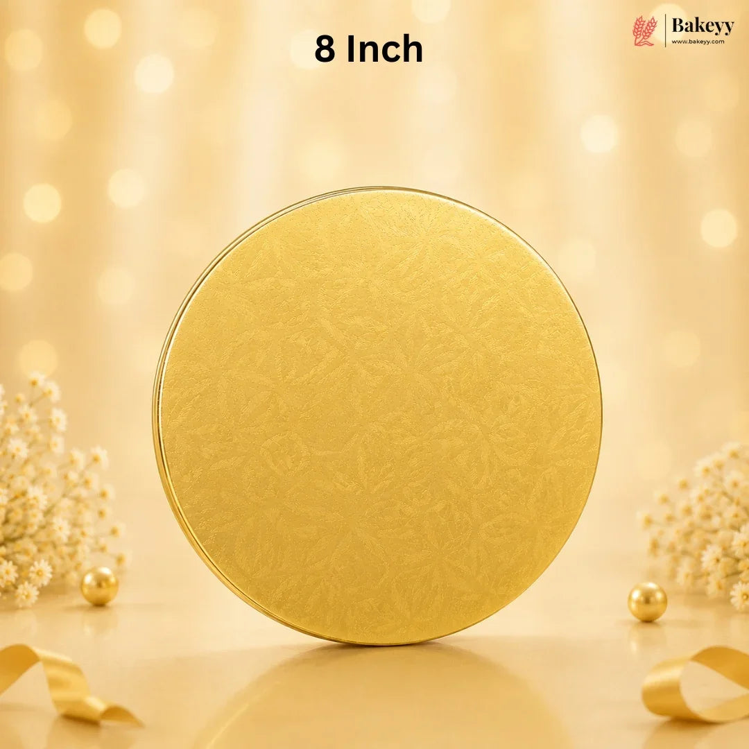 An 8-inch round gold-colored metal tin with a subtle embossed floral pattern, set against a warm, glowing bokeh background with decorative dried flowers and ribbons.