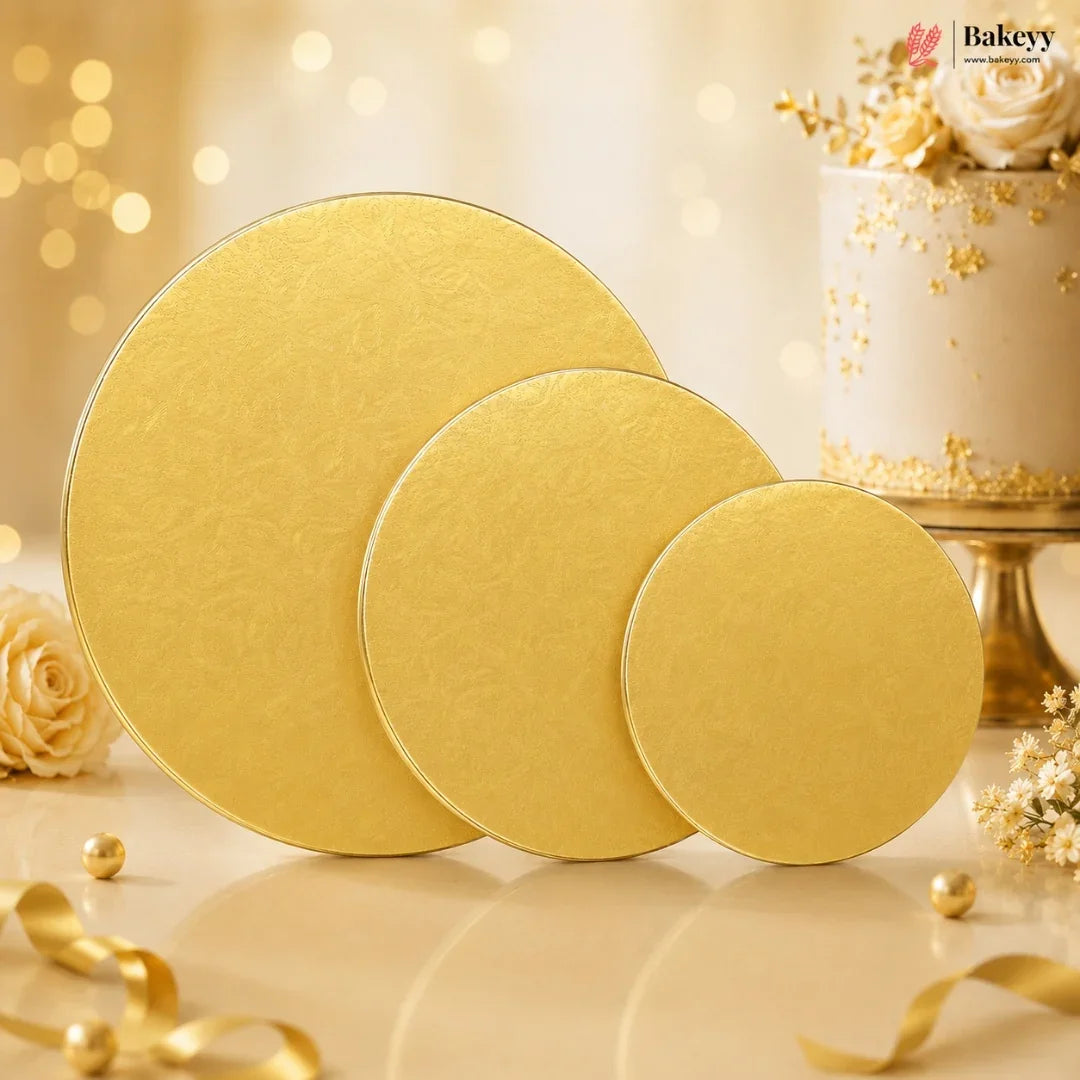 Three round gold cake stands of decreasing sizes arranged on a light surface, with a decorated white cake and gold floral accents in the background. The Bakeyy logo appears in the top right corner.