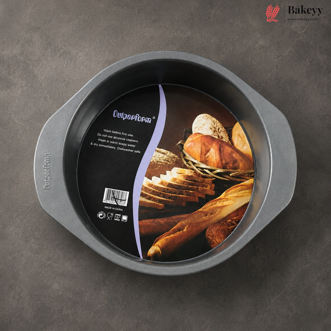 A round non-stick baking pan with side handles, shown from above on a dark gray textured surface. The inside of the pan has a large black product label featuring bread imagery and the brand name 'Cupcake Pan'.