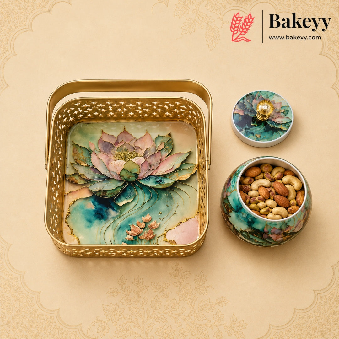 A decorative gold metal gift tray with a lotus pond design, shown alongside a matching lidded container and a small jar of nuts. The Bakeyy brand logo is visible in the top right corner.
