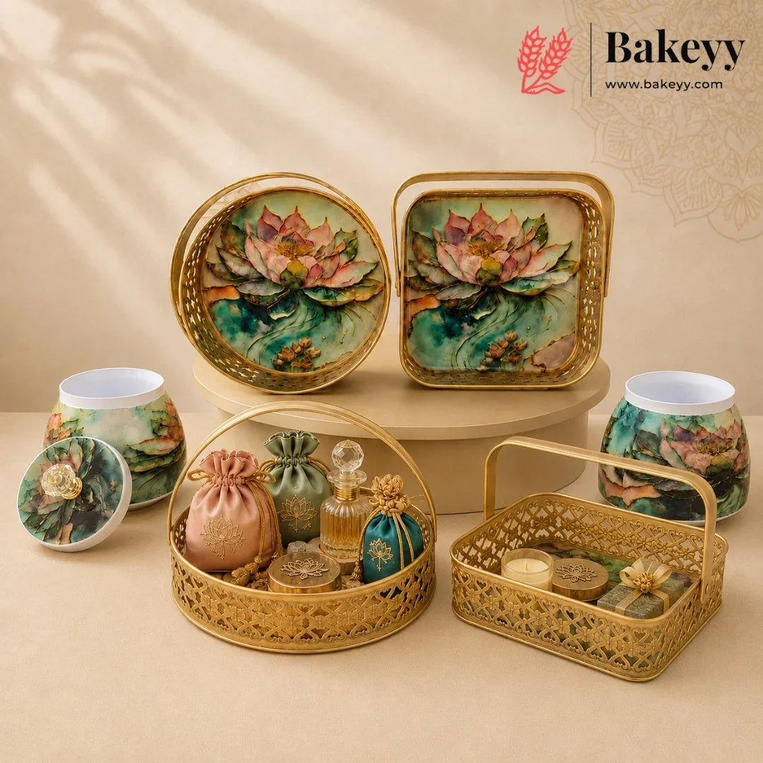 A styled product display of ornate gold-toned metal and ceramic containers with hand-painted lotus flowers, arranged on beige pedestals against a warm beige background. The set includes round and square trays, two lidded jars, a small basket with a handle, and decorative pouches and bottles.