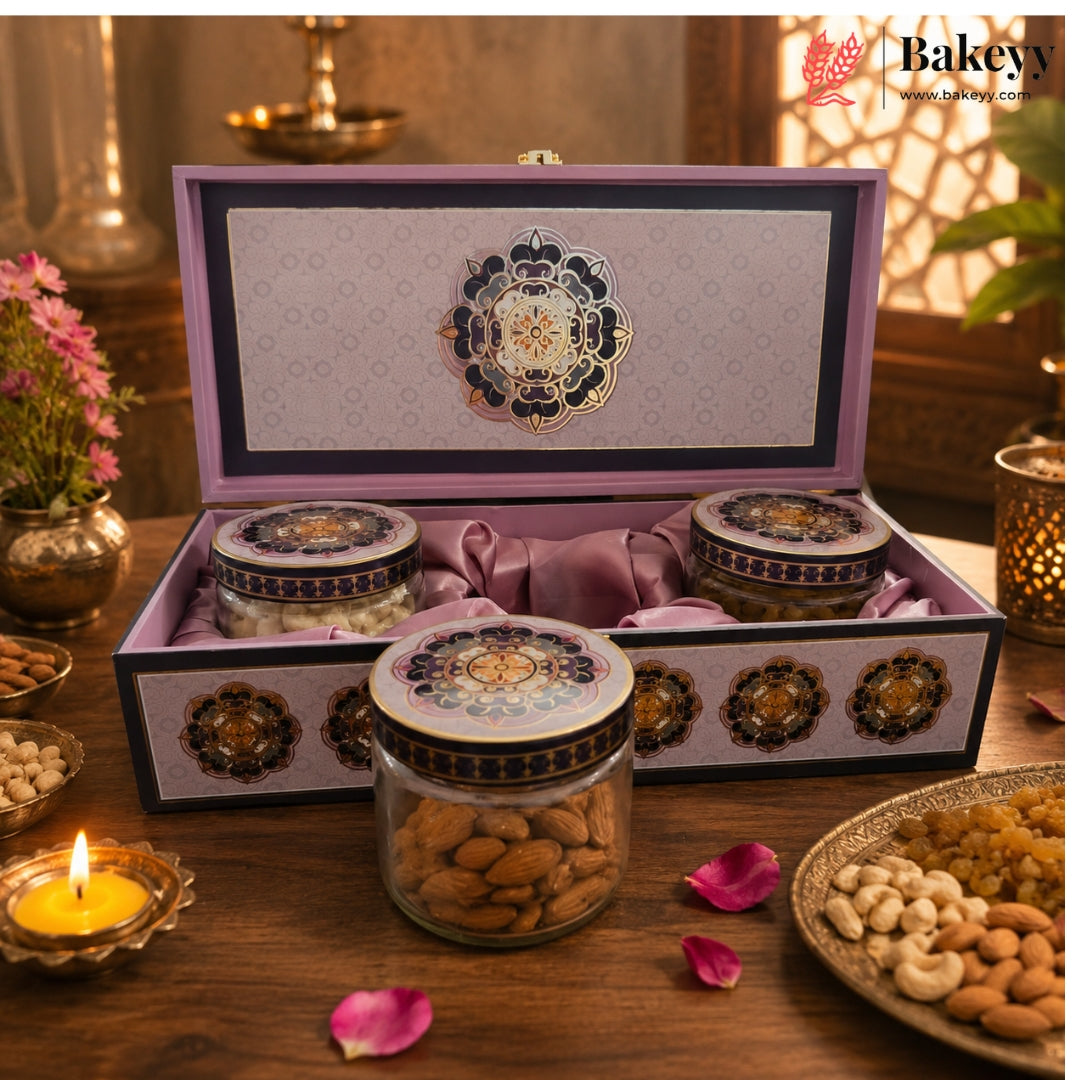 An ornate purple and gold gift box filled with jars of nuts and sweets, displayed on a wooden table with decorative candles, flowers, and plates of almonds, cashews, and raisins.