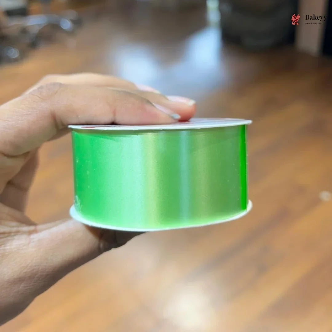 Hand holding a spool of green ribbon on a wooden surface