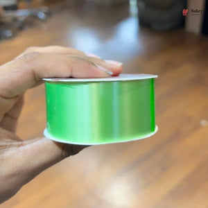 Hand holding a spool of green ribbon on a wooden surface