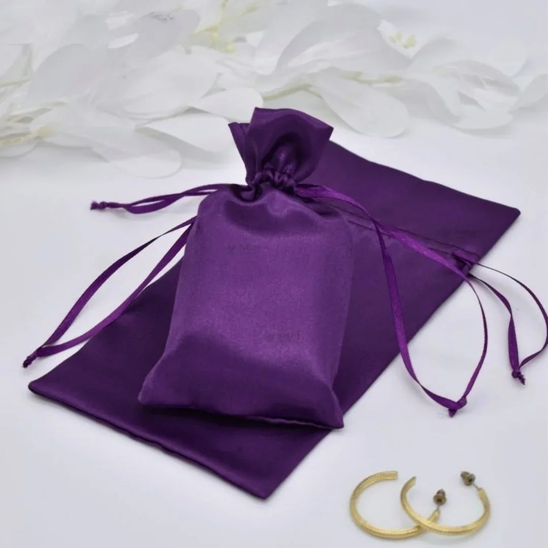 Purple satin drawstring bag on a white background with gold jewelry.