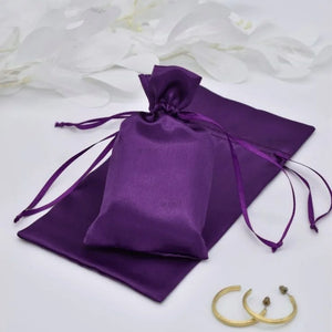 Purple satin drawstring bag on a white background with gold jewelry.