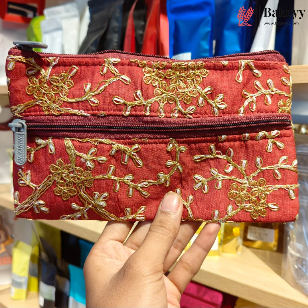 A red quilted fabric pouch with gold floral embroidery and a silver zipper, held by a hand in front of a store background.