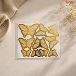 Set of gold butterfly-shaped cookie cutters on a beige surface with a textured fabric and dried flowers in the background.