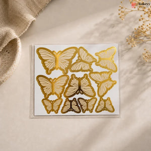 Set of gold butterfly-shaped cookie cutters on a beige surface with a textured fabric and dried flowers in the background.