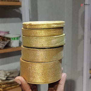 Stack of gold glittery round boxes held by a hand with a blurred background