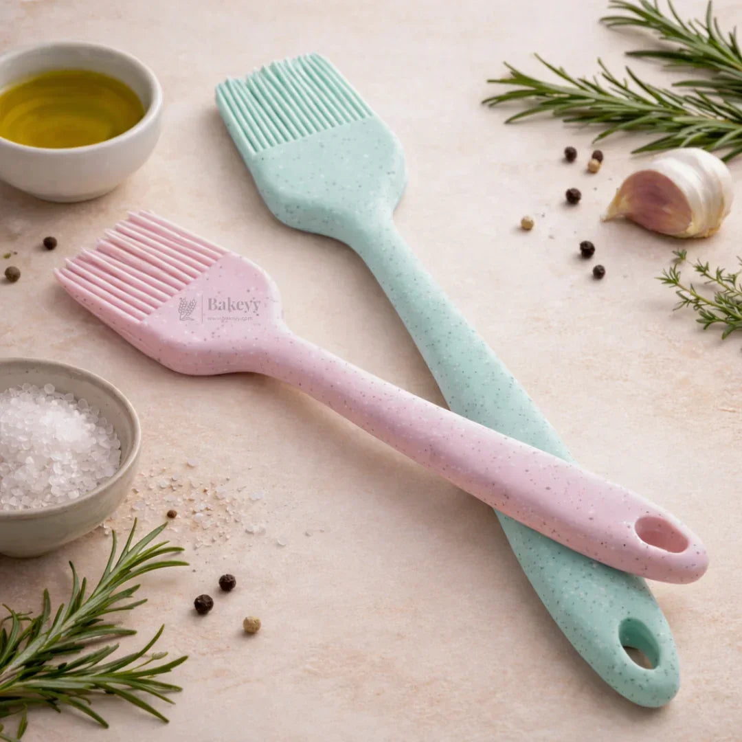 Pastel pink and blue silicone baking brushes on countertop with herbs, salt, oil, Bakeyy.com