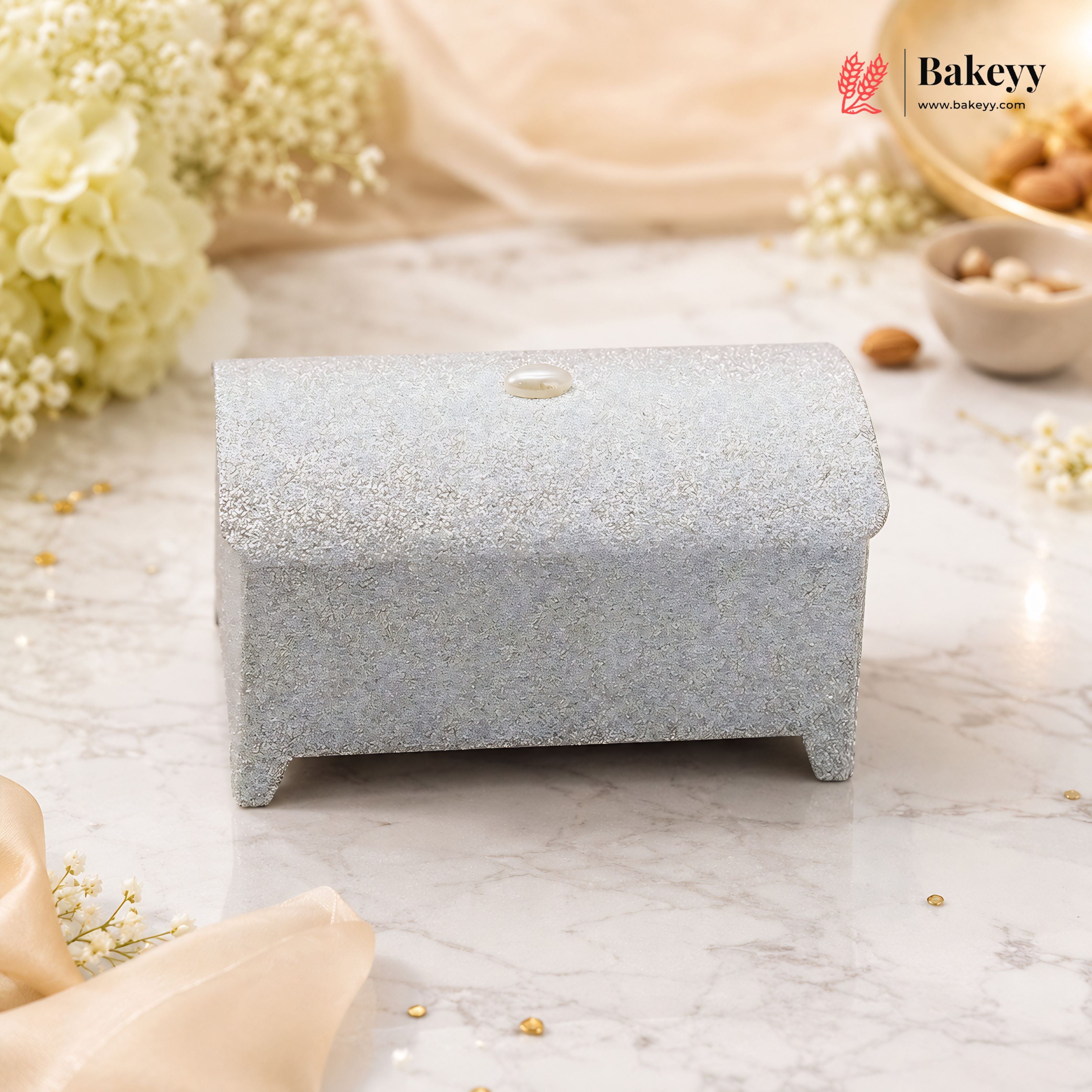 Small decorative box with a textured surface on a marble background with flowers and Bakeyy branding.