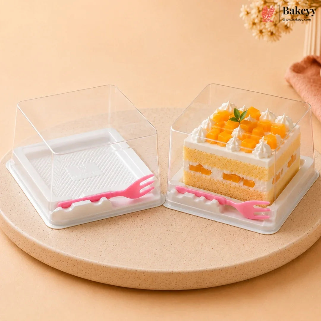 Two clear plastic square cake boxes with white bases and pink plastic forks, shown empty and with a sliced mango cake inside, on a round beige pedestal against a warm beige background.