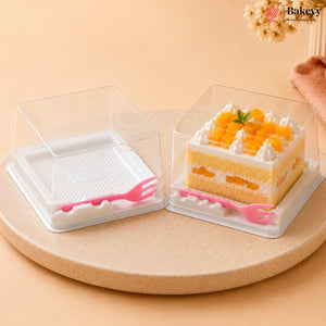 Two clear plastic square cake boxes with white bases and pink plastic forks, shown empty and with a sliced mango cake inside, on a round beige pedestal against a warm beige background.