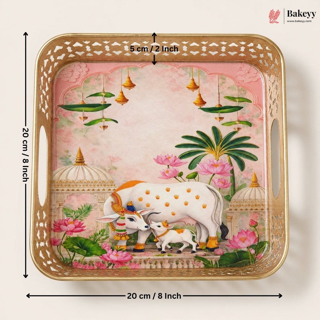 A square decorative tray with a gold-toned perforated border and a pink illustrated scene featuring a white cow and calf, lotus flowers, and green leaves. Black dimension arrows and text show the tray is 20 cm by 5 cm.