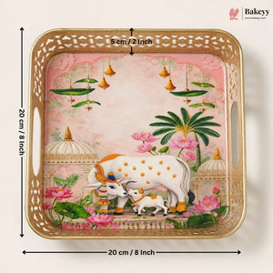 A square decorative tray with a gold-toned perforated border and a pink illustrated scene featuring a white cow and calf, lotus flowers, and green leaves. Black dimension arrows and text show the tray is 20 cm by 5 cm.