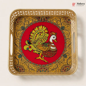 A square decorative tray with cutout handles, featuring a red center with a stylized peacock illustration and an ornate gold paisley border, photographed on a plain light background. The Bakeyy logo appears in the top right corner.