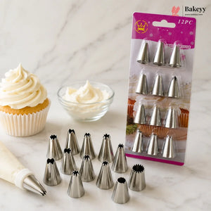 Twelve metal piping nozzles shown with several loose nozzles in front and a packaged set on the right. A piping bag with a nozzle is also visible, along with a frosted cupcake and a small bowl of white icing on a light marble surface.