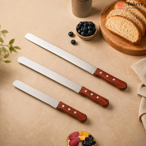 Three long serrated bread knives with reddish-brown wooden handles are arranged diagonally on a beige surface, surrounded by bread, blueberries, and a small cup, with the Bakeyy brand logo in the top right corner.
