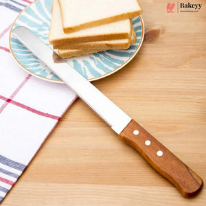 A serrated bread knife with a brown wooden handle and silver stainless steel blade, resting on a light wood table next to a plate of sliced bread and a checkered napkin. The Bakeey brand logo is visible in the top right corner.