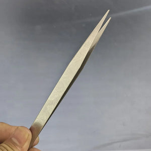 Metal tweezers held by a hand against a gray background